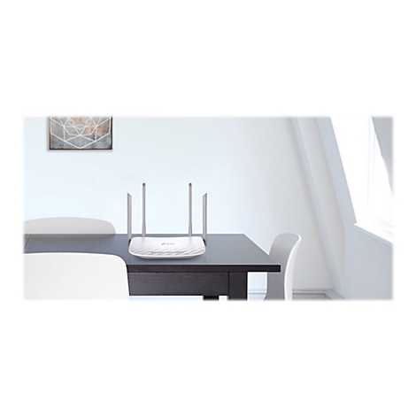 Ein weiÃŸer Router mit vier Antennen steht auf einem dunklen Tisch. Im Hintergrund: StÃ¼hle, ein Bild und ein Fenster.