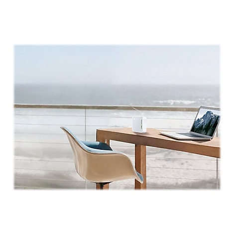 Ein Laptop und ein WLAN-Router stehen auf einem Holztisch, vor dem Meer. Ein Stuhl steht davor.