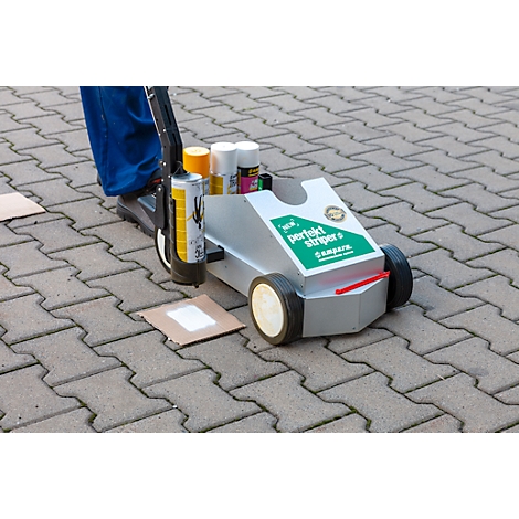 Une personne utilise un chariot pour tracer une ligne. Le chariot est chargé de peinture et porte l'inscription 'perfect striper'.