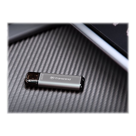 ClÃ© USB grise avec le logo Transcend, posÃ©e sur une surface texturÃ©e. Tablette en arriÃ¨re-plan.