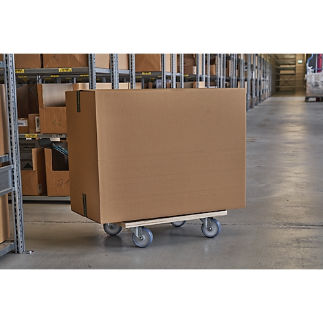 A large cardboard box on a dolly in a warehouse. Shelves with boxes in the background.