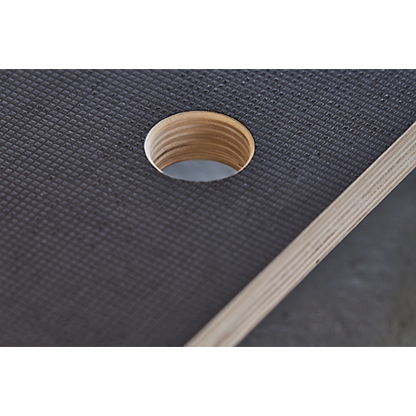 Close-up of a circular hole in a dark, textured material, next to an edge of light wood.