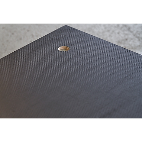 Close-up of a corner of a black table top with a hole. The surface is textured.