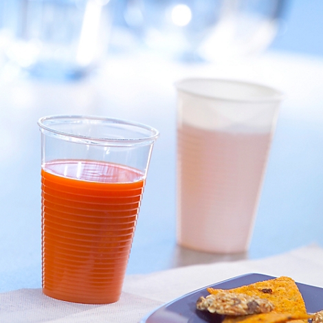 Ein durchsichtiger Plastikbecher mit Orangensaft steht neben einem leeren Becher und einem Teller mit Tortilla-Chips.