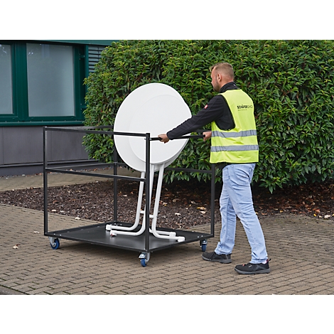Man transports a white folding table on a transport cart. He is wearing a yellow vest.