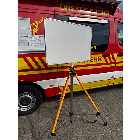 Ein leeres Whiteboard auf einem orangefarbenen Stativ vor einem roten Feuerwehrfahrzeug mit der Aufschrift Einsatzleitung.