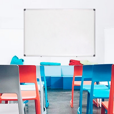 Ein Klassenraum mit weißer Tafel, bunten Stühlen und Polstern.