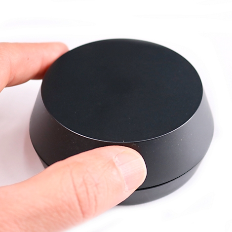 La main tient un objet noir, rond, en forme de cône sur fond blanc.