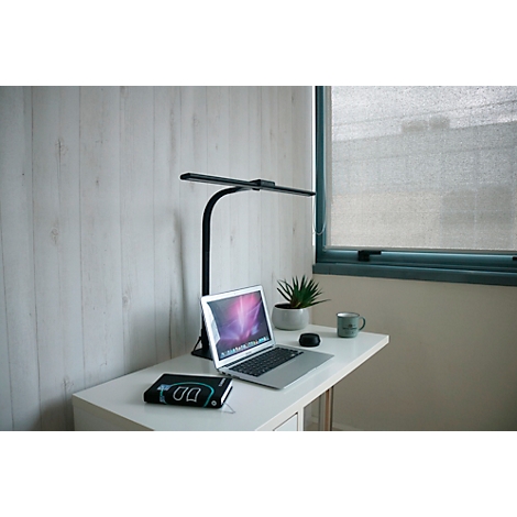 Bureau avec ordinateur portable, lampe, plante et tasse. Fenêtre en arrière-plan, mur aspect bois clair.