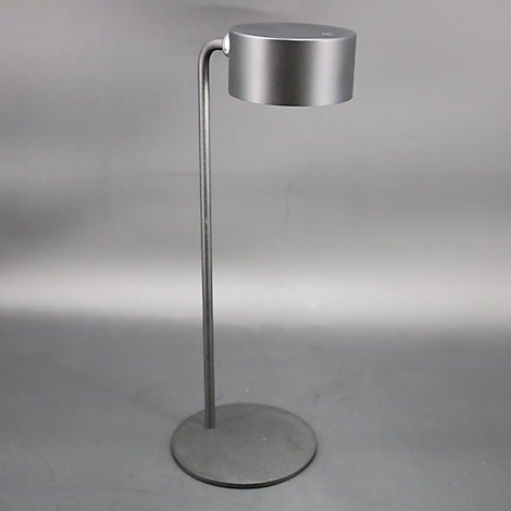 Een zilveren vloerlamp met een ronde voet, een slanke stam en een cilindrische lampenkap.