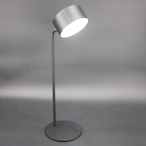 Grijze staande lamp met een cilindrische lampenkap die naar boven is gekanteld. Het licht schijnt fel.