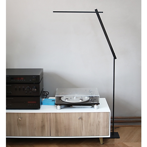 Schlanke, schwarze LED-Stehleuchte steht neben einem Sideboard mit Plattenspieler und Stereoanlage.