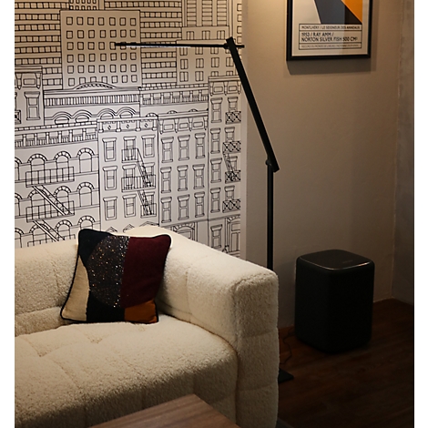 Moderne schwarze Stehlampe neben einem weißen Bouclé-Sofa vor einer illustrierten Stadt-Tapete.