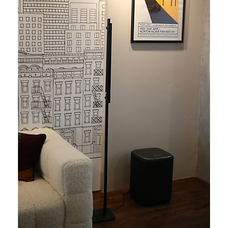Schwarze Lautsprechersäule neben einem Sofa vor einer illustrierten Stadttapete.