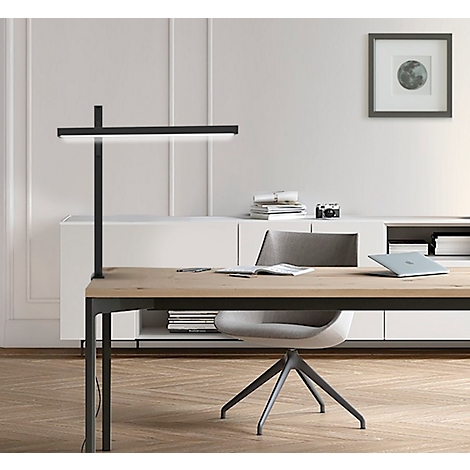 Desk with lamp, laptop, chair, and wall art, bright scene.