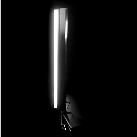 Vertical lamp, silver-colored, with bright light strip in a dark environment.
