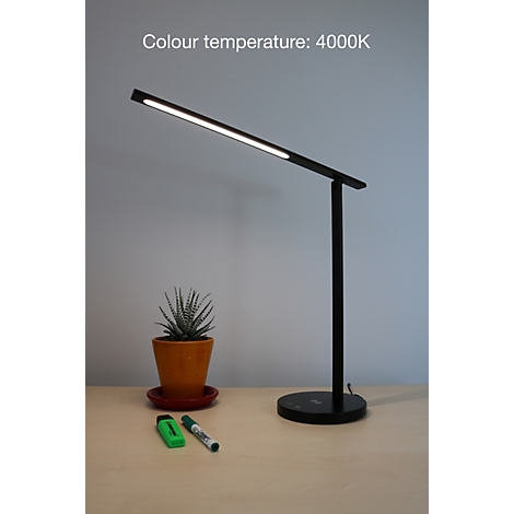 Schlanke, schwarze Schreibtischlampe mit leuchtendem LED-Arm auf einem Holztisch, daneben eine Topfpflanze und Stifte.