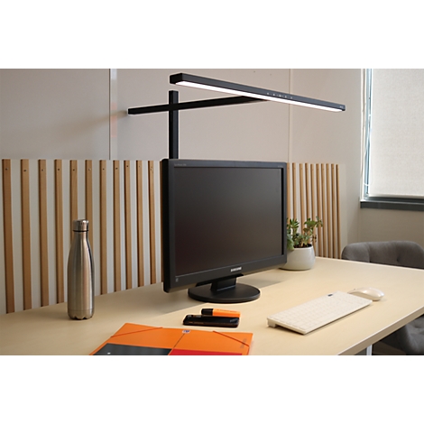 Moderne Schreibtischleuchte über einem Monitor, platziert auf einem hellen Holztisch in einem Büro.