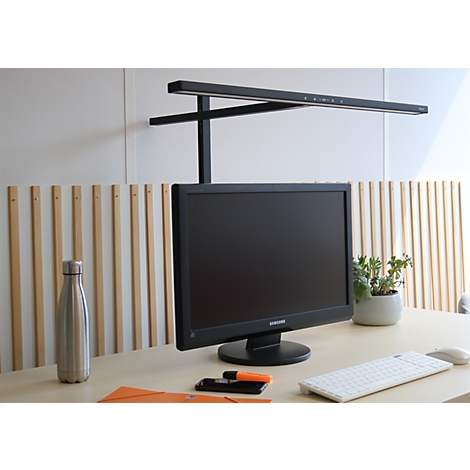 Schwarze Monitor-Lichtleiste auf einem hellen Schreibtisch mit Monitor, Tastatur und einer Metall-Trinkflasche.