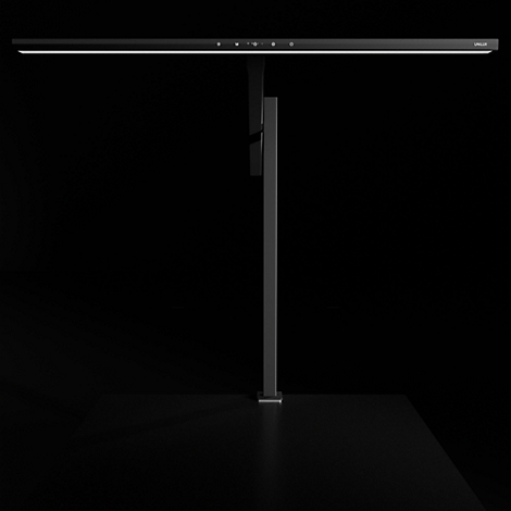 Schwarze, minimalistische Schreibtischlampe vor dunklem Hintergrund.