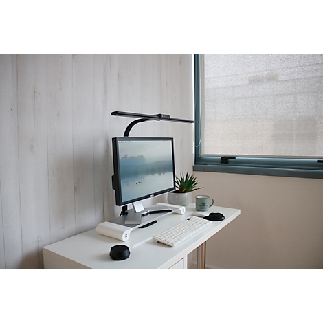 Schreibtisch mit Monitor, Tastatur, Lampe und Pflanze vor Holzpaneelen.