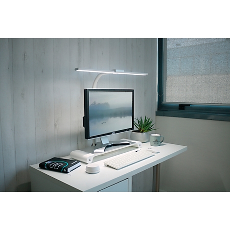 Schreibtisch mit Computer, Lampe, Pflanze und Kaffeetasse. Helle, minimalistische Arbeitsumgebung.