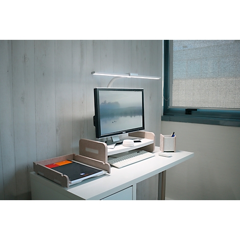 Schreibtisch mit Monitor, Lampe, Ablage und Stiftehalter. Im Hintergrund ein Fenster.