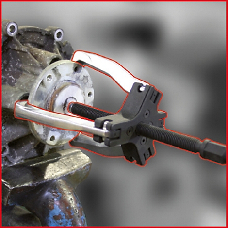 Ein silbernes Werkzeug greift in ein mechanisches Bauteil. Der Hintergrund ist unscharf.