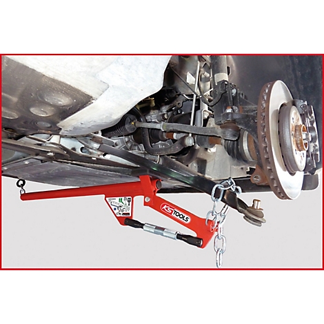 Nahaufnahme eines roten Werkzeugs unter einem Autoreifen. Das Werkzeug ist mit einer Kette am Radaufhängungsteil befestigt.