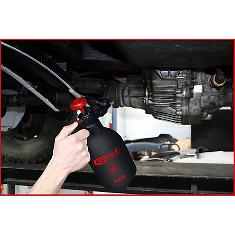 Person besprüht Fahrzeugunterboden mit einer schwarzen Sprühflasche. Aufschrift: KS TOOLS, 2L.