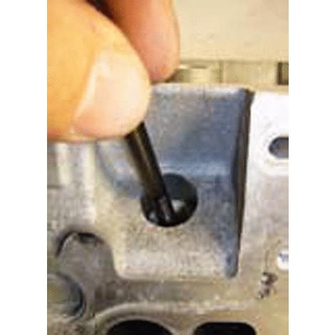 Ein Finger führt einen schwarzen Stab in ein Loch in einem grauen Metallteil.