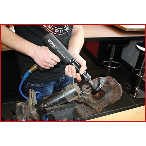 Eine Person benutzt einen Druckluftschrauber, um an einem Radaufhängungsteil zu arbeiten.