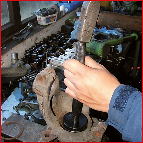 Hand mit Hammer schlägt auf Werkzeug. Werkzeug wird in ein Autoteil geschlagen.