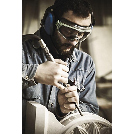 Un homme sculpte la pierre avec des lunettes de sécurité et une protection auditive. Il travaille concentré sur une œuvre d'art ornée.