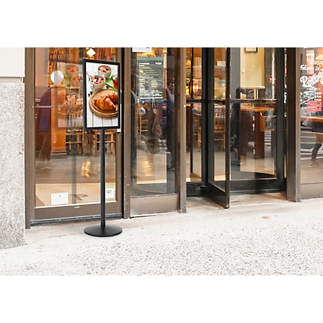 Schwarzes Menüschild vor einem Restaurant. Ein Menü mit Speisen ist abgebildet. Durch die Tür sieht man das Innere des Restaurants.