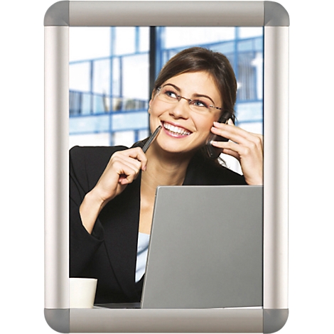 Une femme souriante dans un bureau, portant des lunettes et un stylo dans la bouche. Elle téléphone et regarde en l'air.