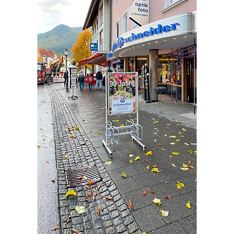 Support à vélos devant un magasin avec l'inscription "Optik Foto Schneider" et une enseigne publicitaire pour un 90e anniversaire.