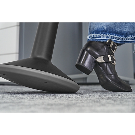 Black leather shoe with silver buckle and a chair leg. The shoe is visible on the foot. In the background a grey carpet.