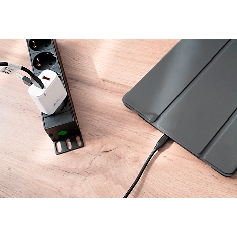 A black power strip with a white charger plugged in. A black cable connects to a gray tablet.