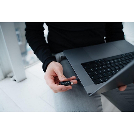 Persoon steekt een USB-stick in een laptop. Heldere ramen op de achtergrond.