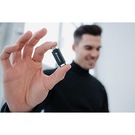 Een man houdt een zwarte Verbatim USB-stick in zijn hand, hij glimlacht.