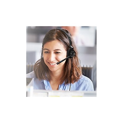 Eine lächelnde Frau mit Headset im Büro, sie schaut auf ihren Computer.