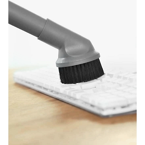 A gray vacuum brush cleans the keys of a white keyboard.