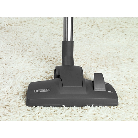 Dark grey vacuum cleaner attachment by Thomas on white carpet. The vacuum head and tube are visible.