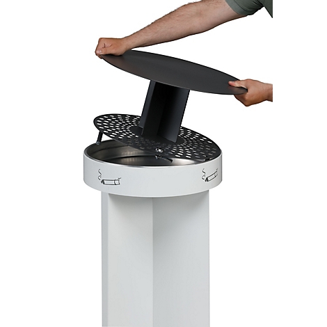 Persoon tilt het deksel van een witte, zeshoekige asbak op. Sigaretsymbolen zijn afgebeeld op de asbak.