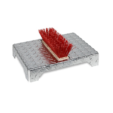 Een metalen voetmat met een traanplaatpatroon. Een rode schoenenborstel is op de mat geplaatst.