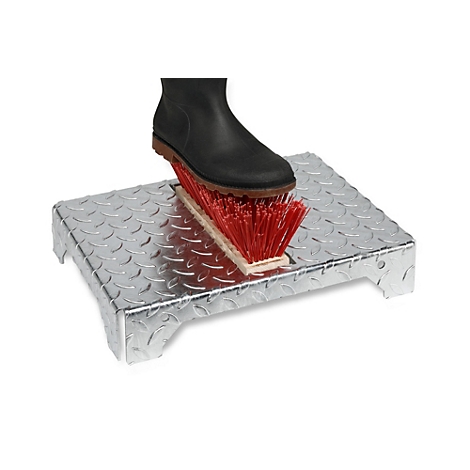 Een zwarte laars stapt op een metalen platform met een ingebouwde rode schoenborstel. De achtergrond is wit.