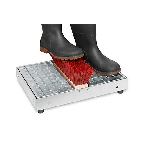 Zwarte rubberen laarzen reinigen hun zolen met een roodharige schoenenborstel op een metalen schoenenschraper.