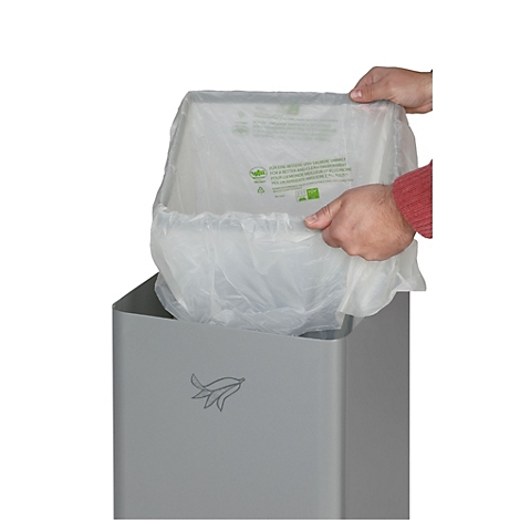 Hände legen einen Beutel in einen grauen Mülleimer. Der Beutel ist durchsichtig mit grünen Texten und Logo.