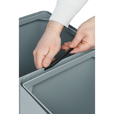 Hände legen schwarze Dichtung in grauen Mülleimer.